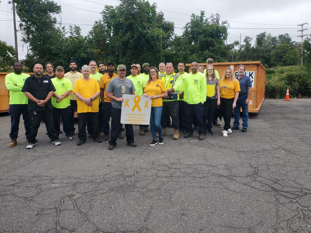 Volunteers in neon shirts pose outdoors holding a Childhood Cancer Awareness Month sign.